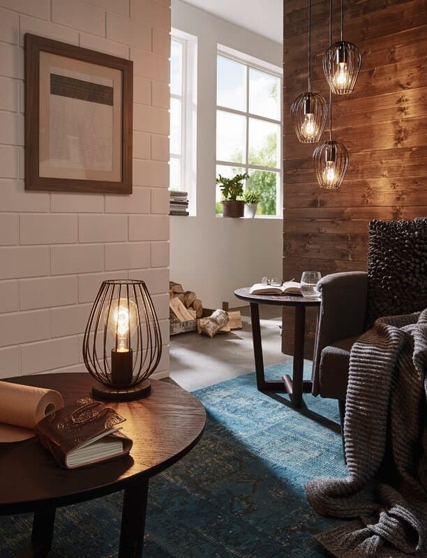 Cozy interior with a wooden table, stylish lamp, armchair, and hanging lights, featuring a textured rug and framed artwork.