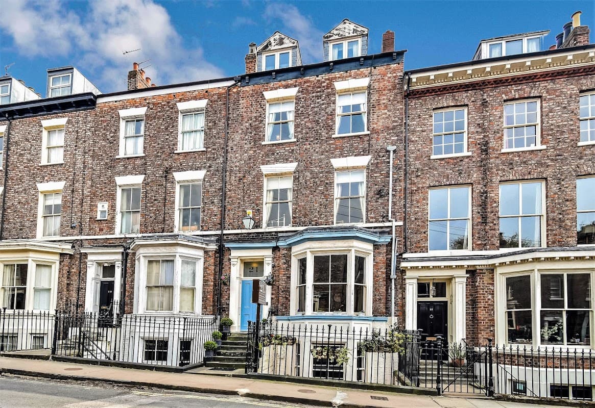 Victorian-style brick building with blue door, large windows, and flower pots, located on a street in York, Yorkshire.