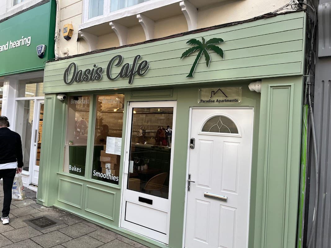 Green exterior of Oasis Café featuring a palm tree logo, door, and windows, with nearby shops visible.