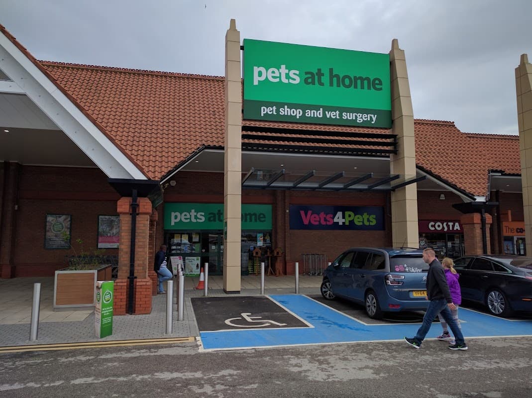 Pet shop entrance with "pets at home" and "Vets4Pets" signs, parking spaces, and shoppers approaching the store.