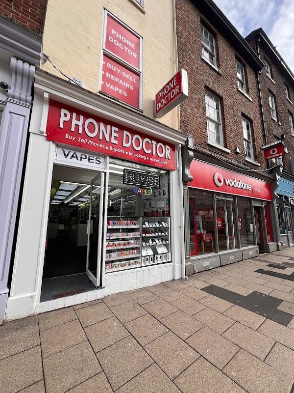 "Storefront of Phone Doctor with signage, displaying phones and vapes, next to a Vodafone store in York."