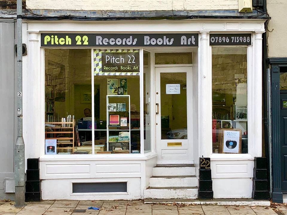 Storefront of Pitch 22 featuring records, books, and art, with large windows and a welcoming entrance.