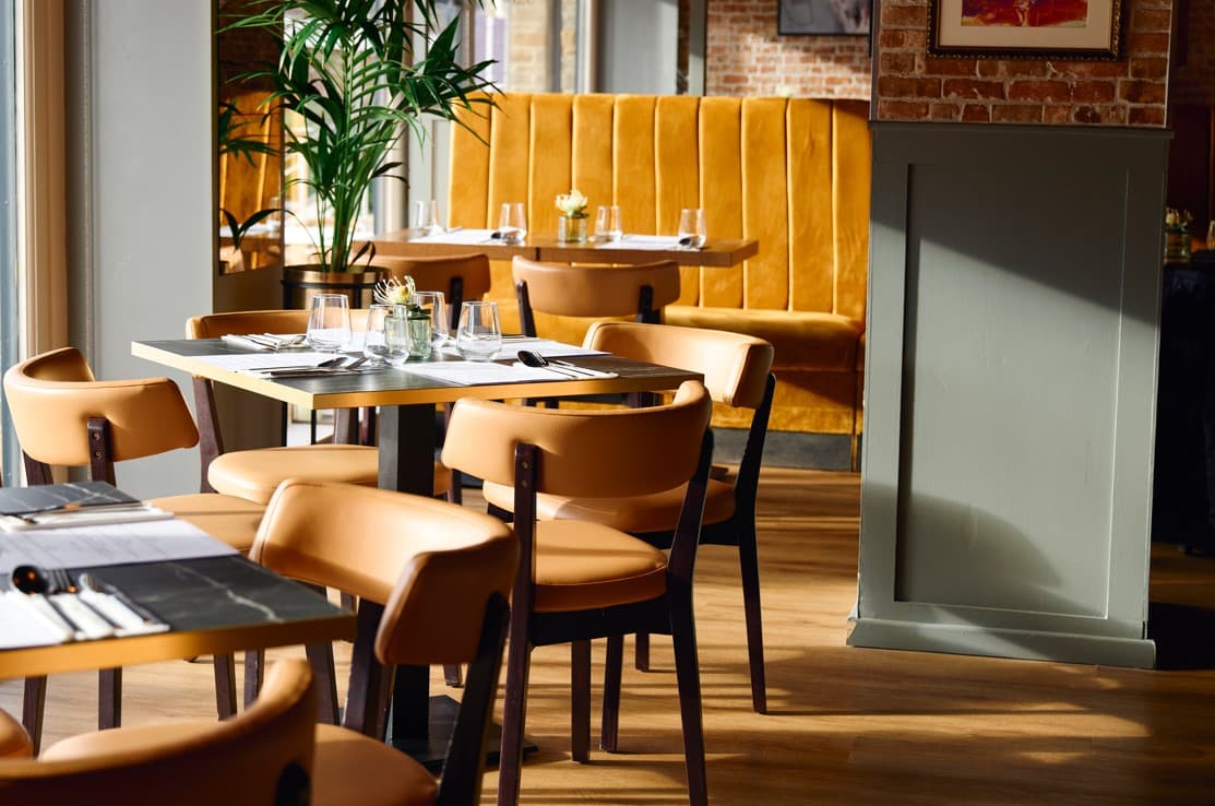 Stylish restaurant interior with wooden floors, orange chairs, and a cozy booth against a brick wall.