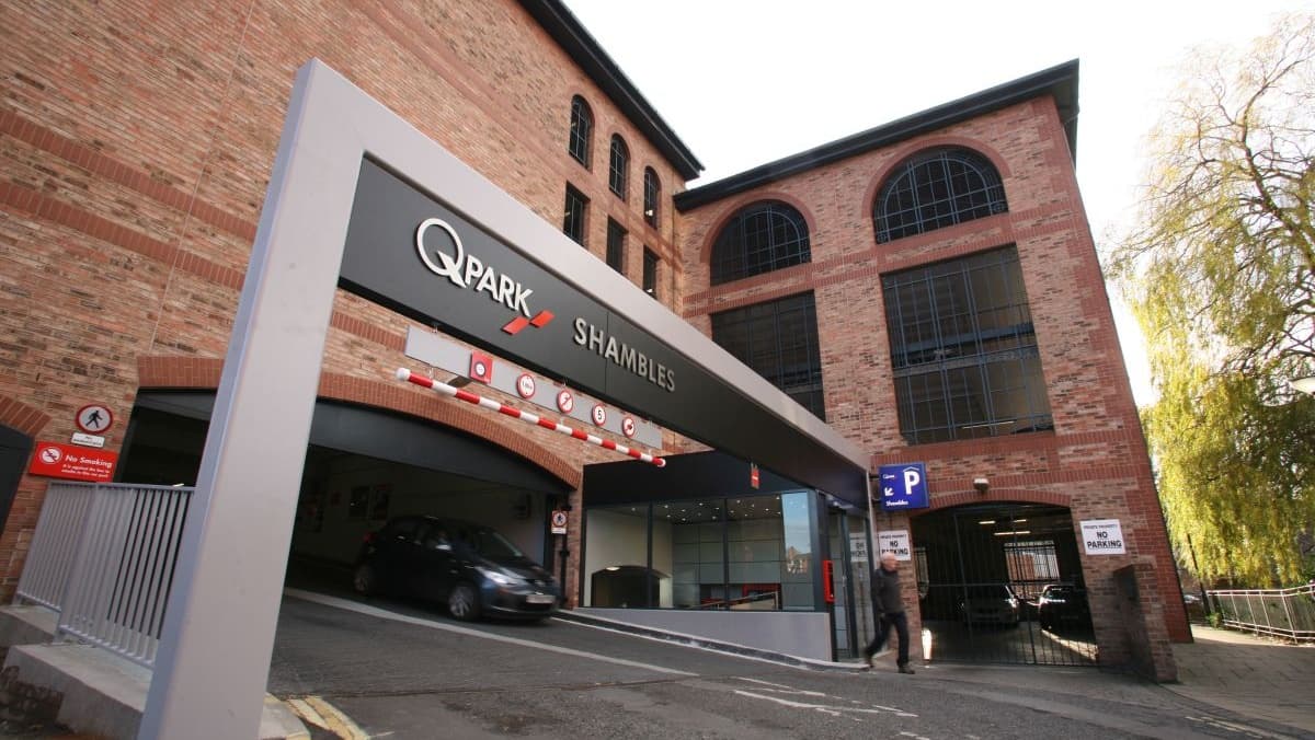 Entrance to Q-Park Shambles with a modern sign, brick building, and a car entering the parking facility.