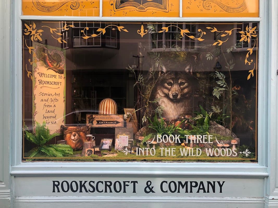 Bookshop window display featuring a wolf, lion, and nature-themed decor with "Welcome to Rookscroft" sign.