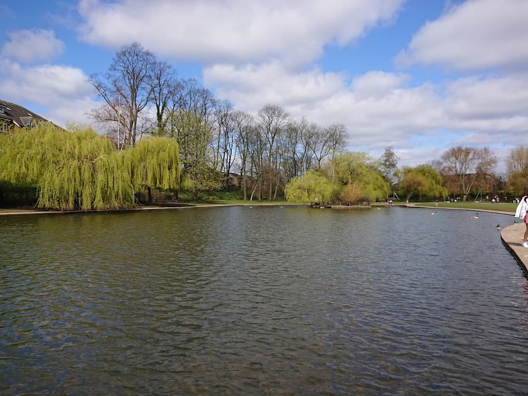 Serene lake surrounded by lush trees and a cloudy blue sky at Rowntree Park in York, Yorkshire.
