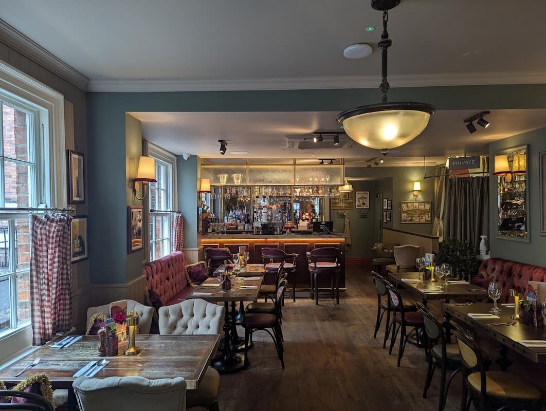 Elegant restaurant interior with wooden floors, cozy seating, a bar with glassware, and decorative wall art.