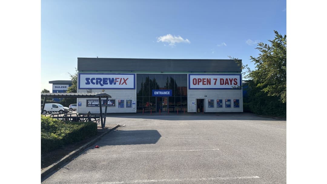 Screwfix storefront with large signs, "OPEN 7 DAYS" and "ENTRANCE," surrounded by a parking lot and greenery.