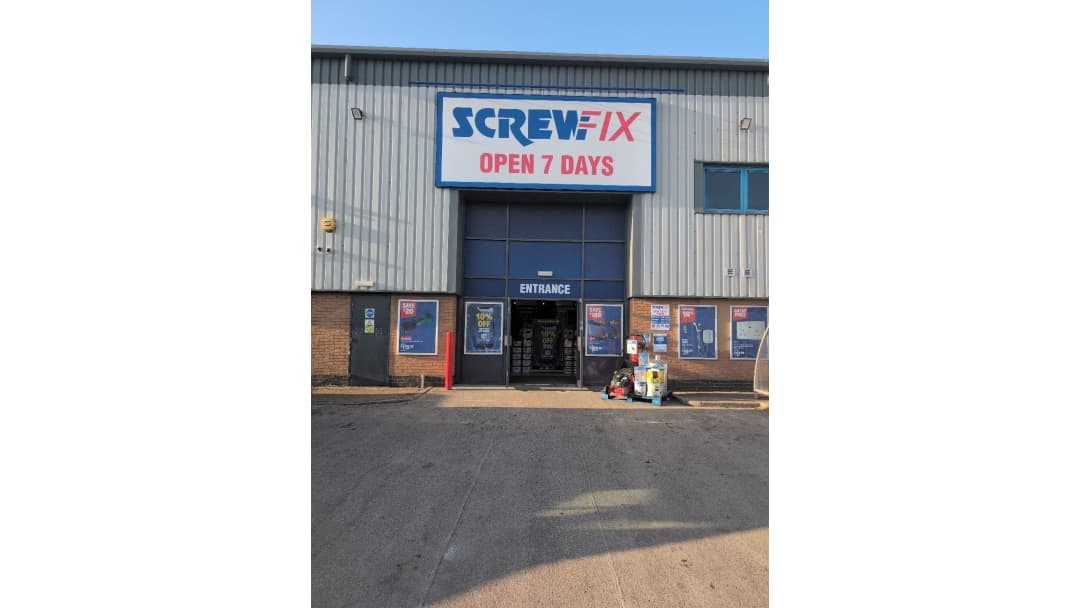Screwfix store with a large sign, open 7 days, featuring an entrance and promotional posters outside.