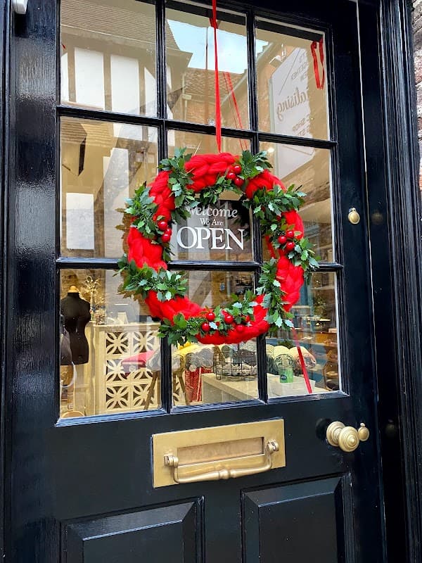 A festive wreath with red ribbons and greenery hangs on a black door with a sign that reads "Welcome, We Are OPEN."