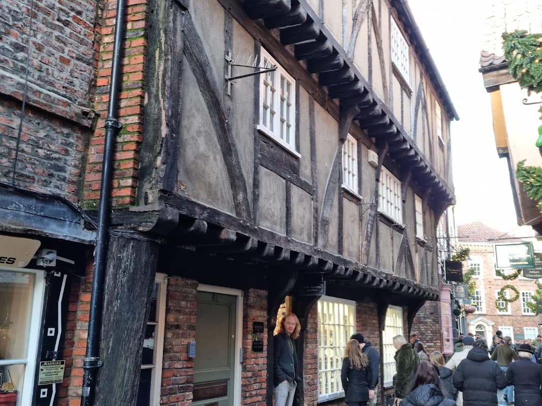 Historic timber-framed building with shopfront, people walking by, and festive decorations in York's Shambles area.