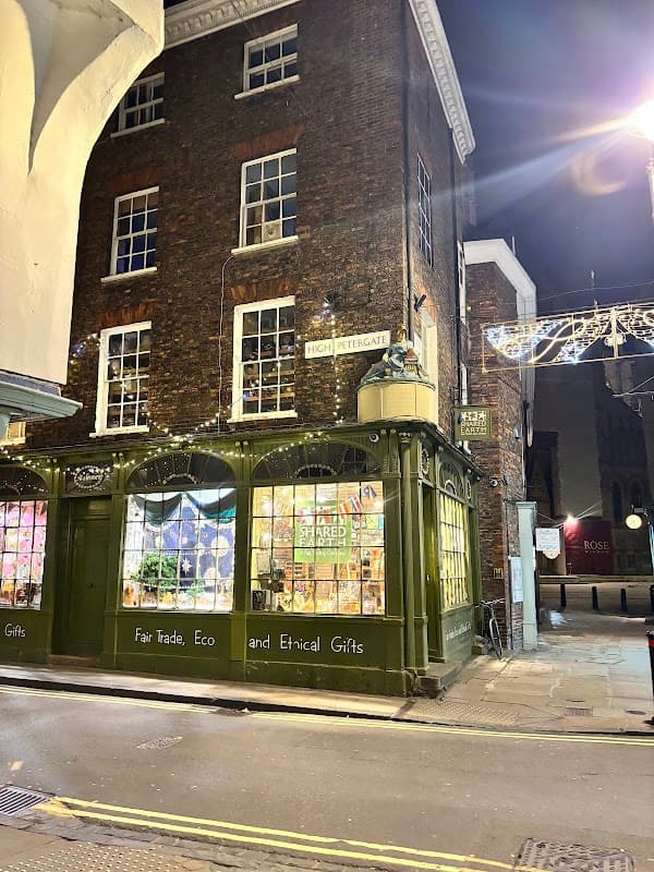 Charming gift shop with green façade, fairy lights, and colorful displays, located on a cobblestone street at night.