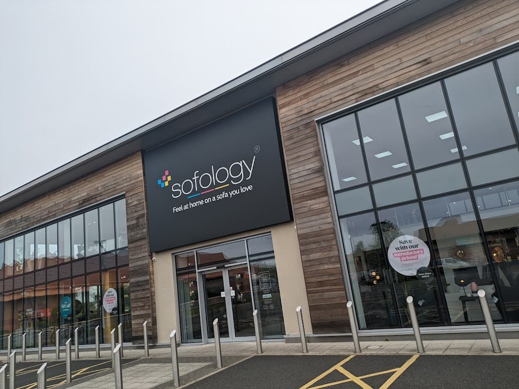 Modern furniture shop with large glass windows and a wooden facade, featuring a prominent sign for Sofology.
