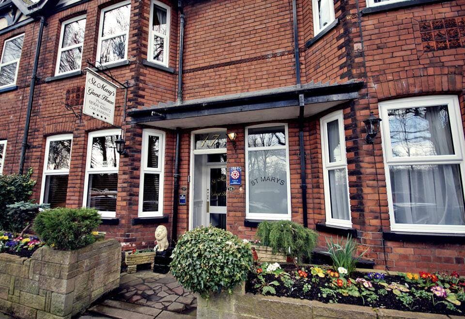 Brick facade of St Mary's Guest House in York, featuring a welcoming entrance and colorful flower beds.