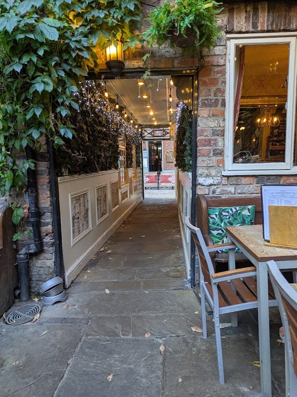 Charming stone pathway leading to a cozy restaurant with greenery and warm lighting, inviting outdoor seating.