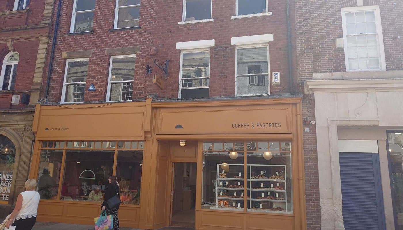 The Cornish Bakery storefront features a warm orange facade, large windows, and displays of pastries inside.