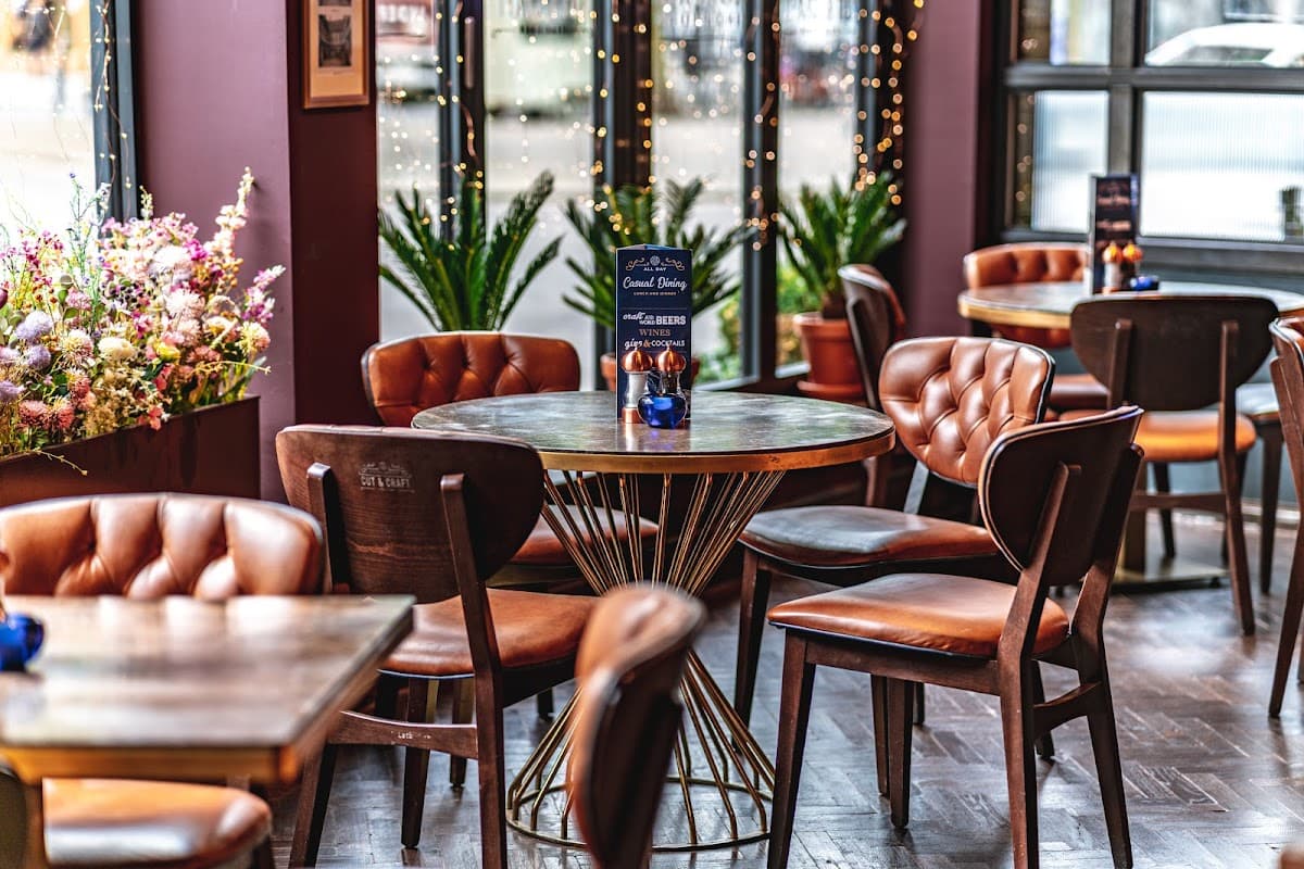 Cozy dining area with wooden tables, leather chairs, potted plants, and soft lighting, creating an inviting atmosphere.