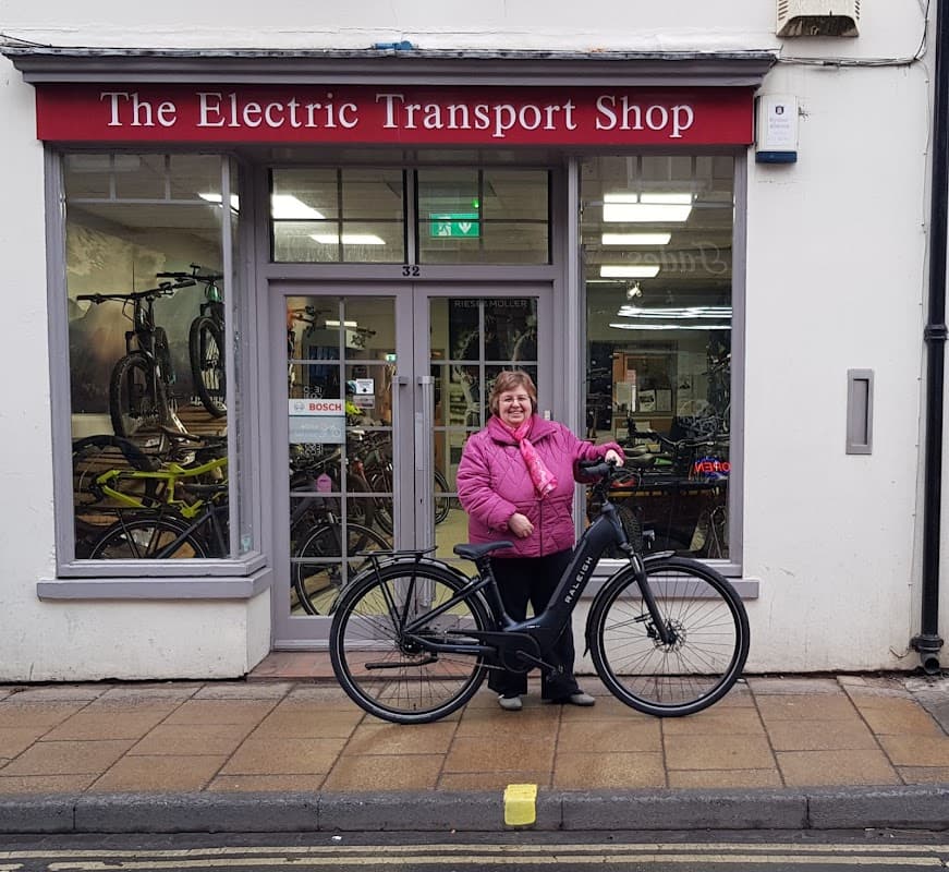 A woman in a pink jacket stands next to an electric bike outside The Electric Transport Shop in York.