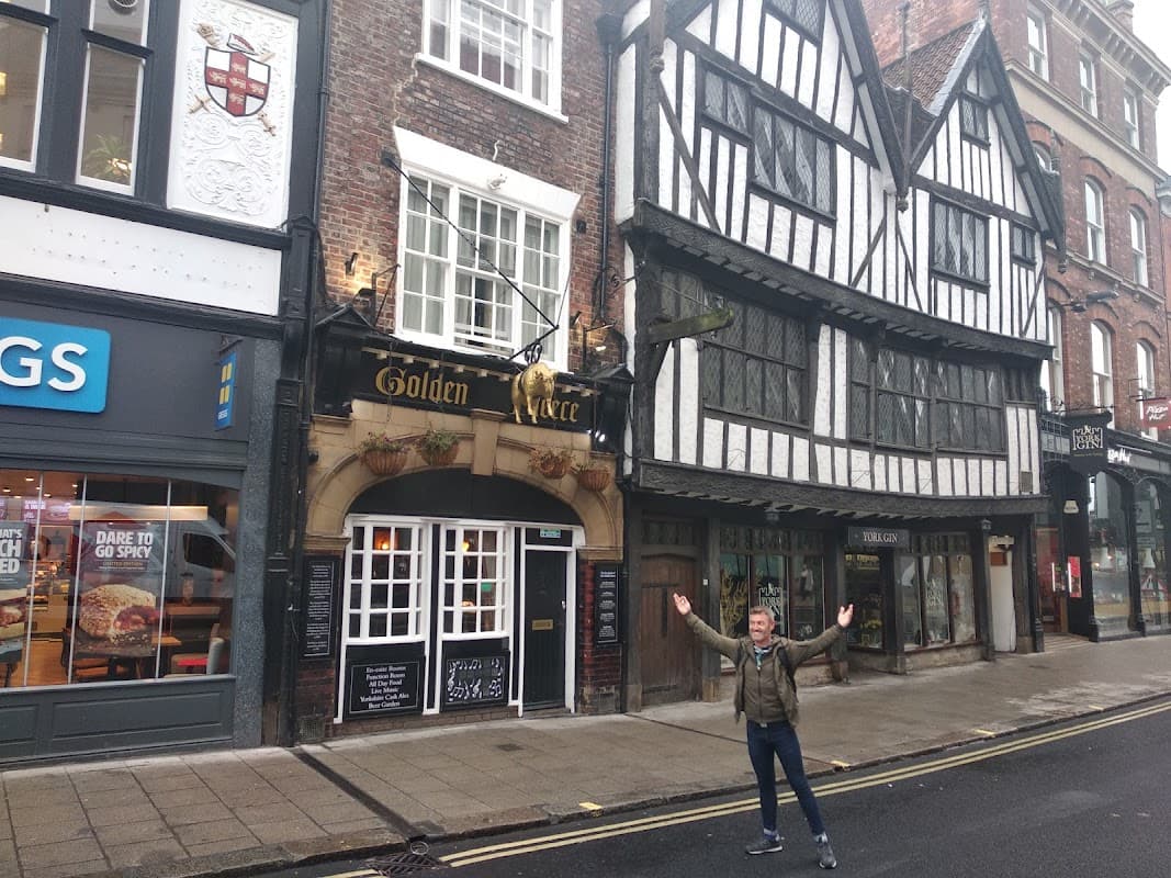 Historic pub with timber-framed architecture, signage for "Golden Fleece," and a person standing with arms outstretched.