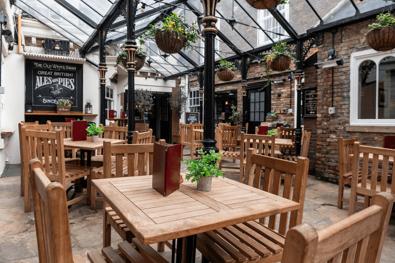 Quaint pub courtyard with wooden tables, chairs, and potted plants under a glass roof in York.