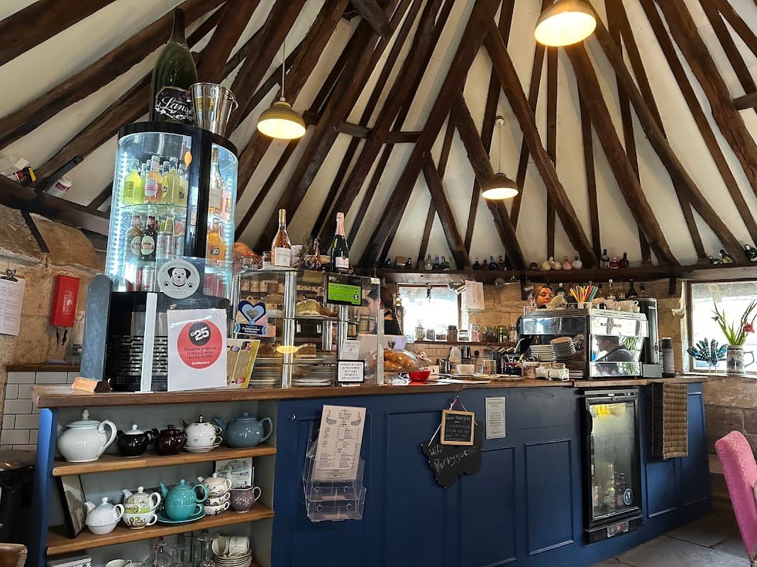 Cozy cafe interior with wooden beams, a blue counter, display of drinks, and various teapots on shelves.
