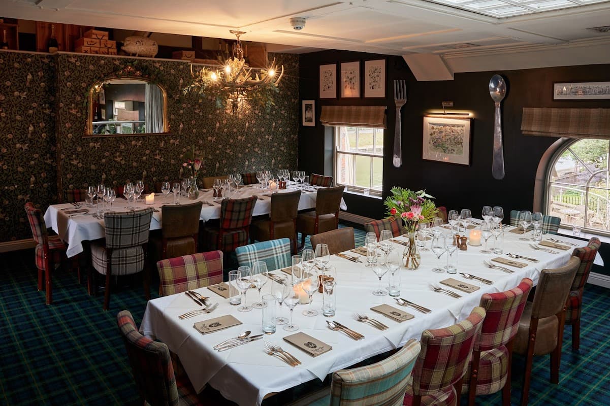 Elegant dining setup with checkered chairs, white tablecloths, and floral wallpaper in a cozy restaurant interior.