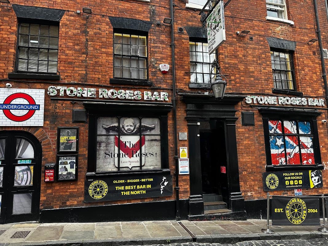 Red brick pub facade with "Stone Roses Bar" signage, posters, and a round sign reading "Underground."