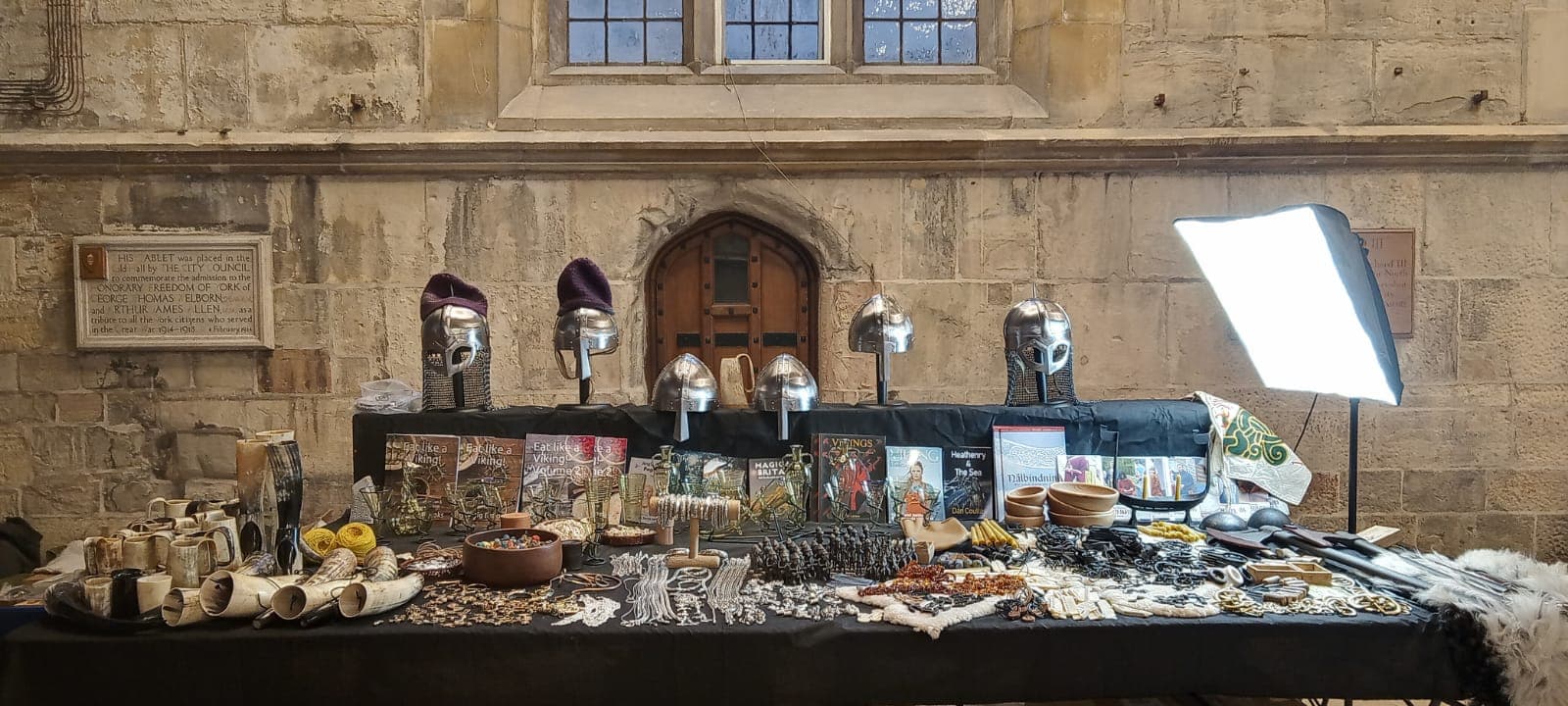 Viking-themed crafts and jewelry displayed on a table, featuring helmets, pottery, and decorative items in a historic setting.