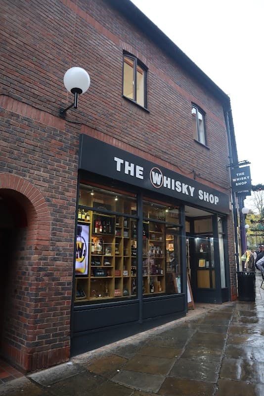 Brick building with large windows displaying various whisky bottles and a sign reading "The Whisky Shop."