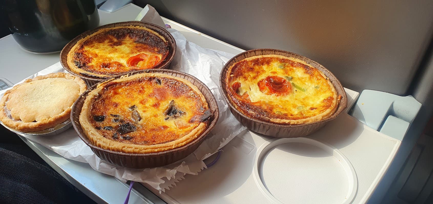 Three savory pastries on a tray, including a quiche and a pie, with golden crusts and colorful toppings.
