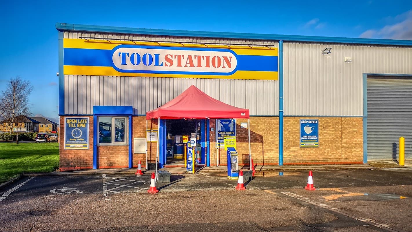 Bright blue and yellow storefront with a red canopy, signage for Toolstation, and parking cones outside.