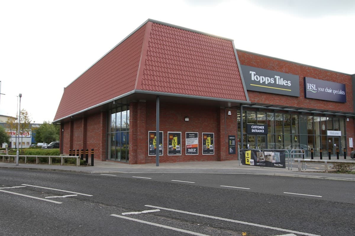 Brick building with a red tiled roof, large windows, and signage for Topps Tiles and HSL. Parking area visible.