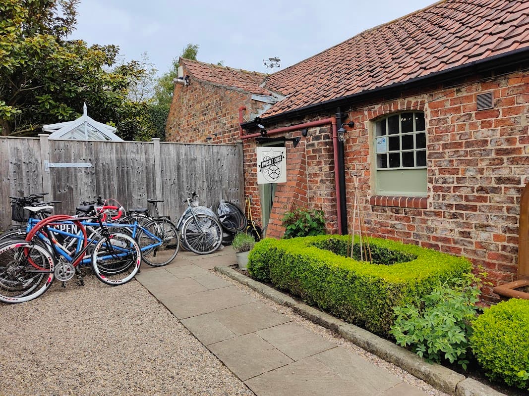 Bicycles parked outside a rustic brick building with a sign for "Twisted Cogs" and neatly trimmed hedges.