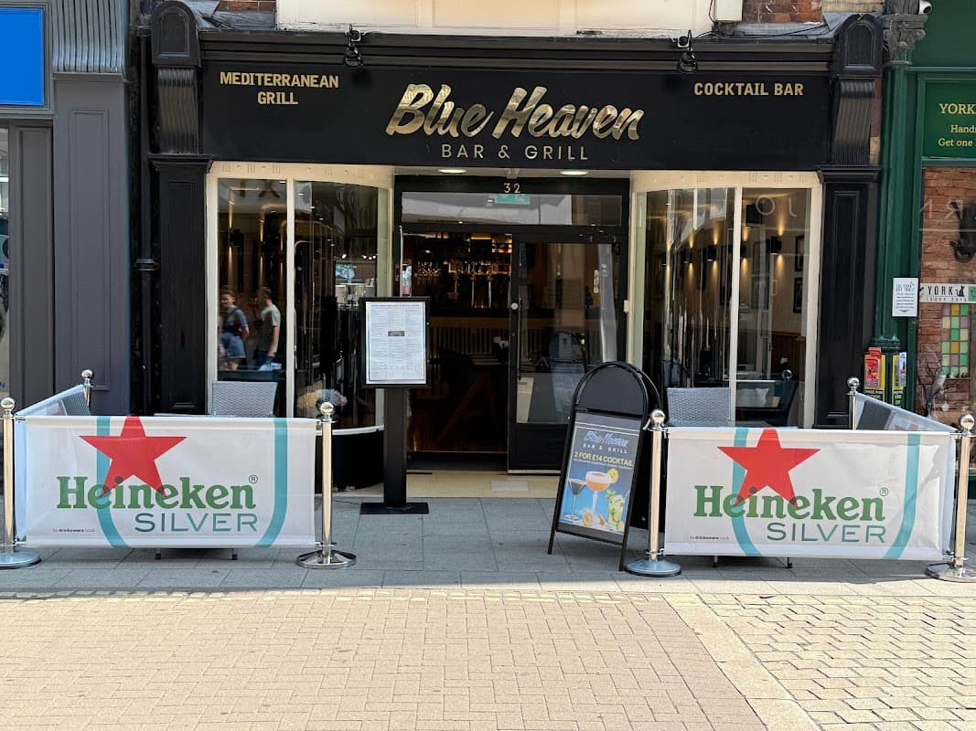 Entrance to Blue Heaven Bar & Grill featuring outdoor seating, Heineken banners, and a menu display.