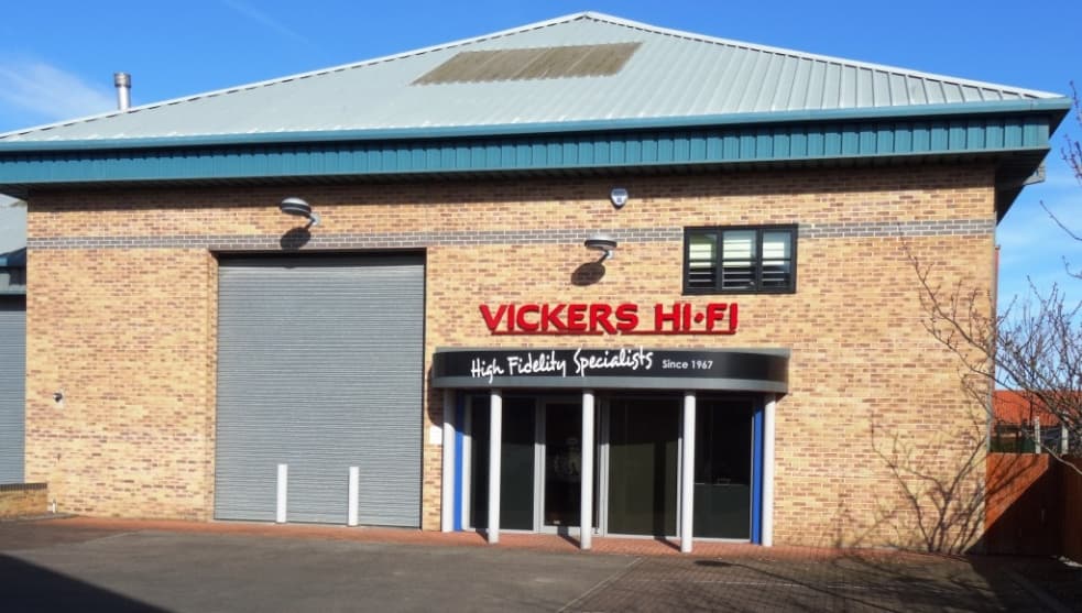 Vickers HiFi storefront with a large sign, modern architecture, and a roll-up door under a clear blue sky.