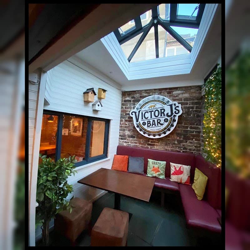 Cozy pub interior featuring a sign for "Victor J's," a wooden table, colorful cushions, and a skylight.