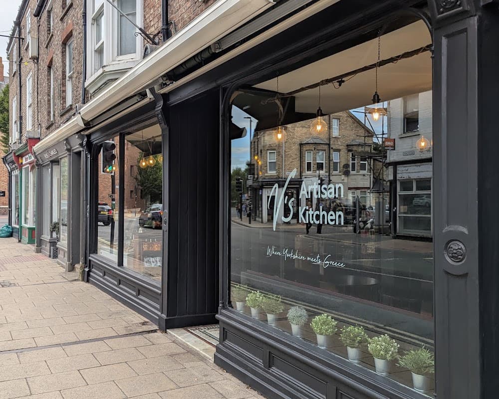 V's Artisan Kitchen storefront with large windows, hanging lights, and potted plants along the sidewalk in York.