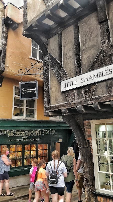 Historic timber-framed buildings along a narrow street, with a jewellers' shop and visitors exploring the area.