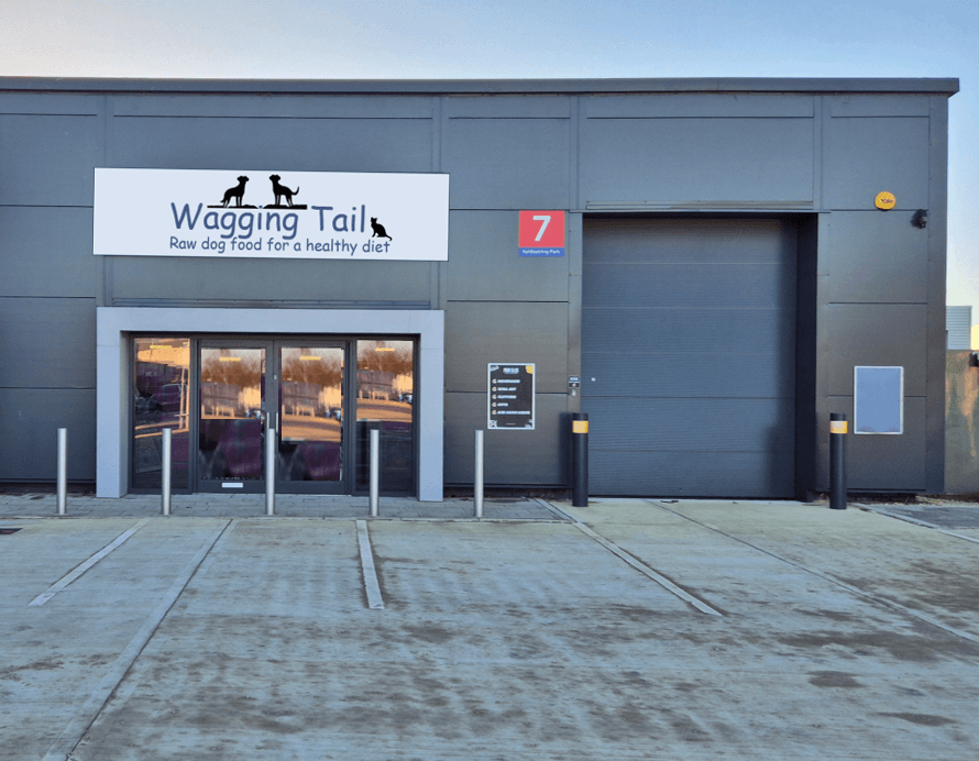 Entrance of Wagging Tail Raw Dog Food shop with a large sign, parking area, and a loading dock in York, Yorkshire.
