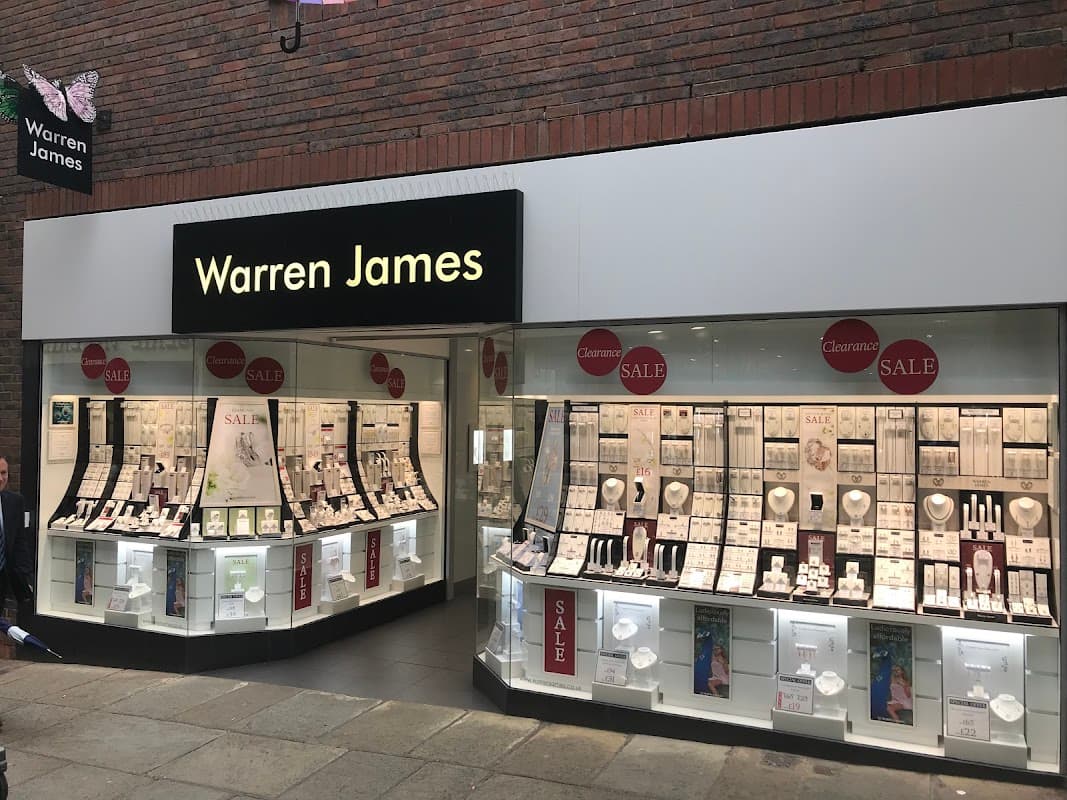 Jewelry store exterior with large "Warren James" sign, display windows featuring various jewelry pieces and sale signs.