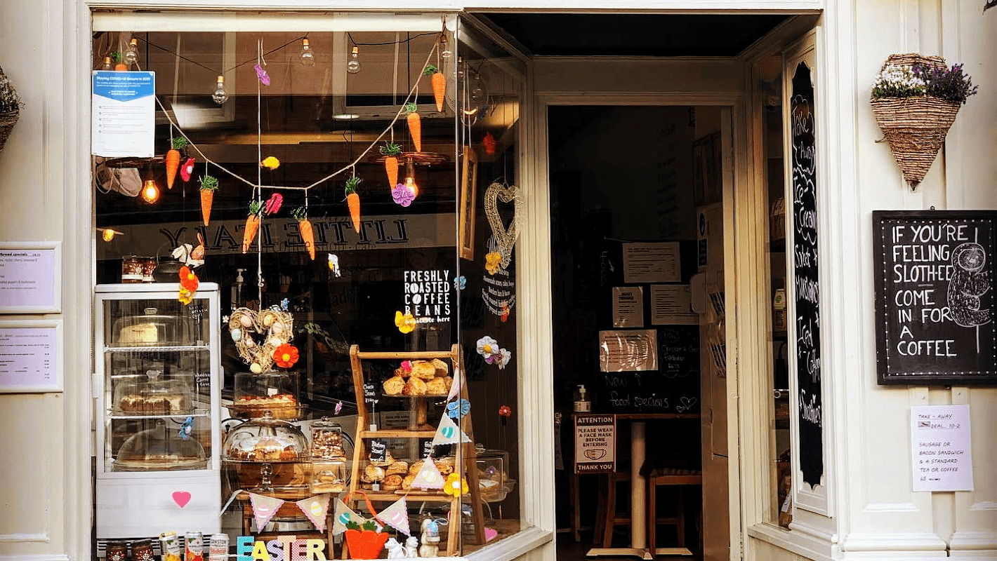 Charming café entrance with colorful decorations, baked goods display, and a welcoming sign for coffee.