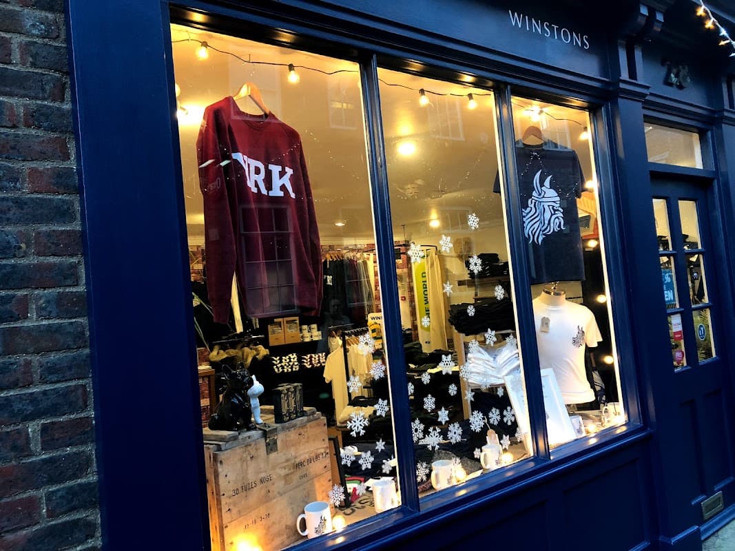 Clothing shop window featuring sweatshirts, t-shirts, and decorative items with lights and snowflake accents.