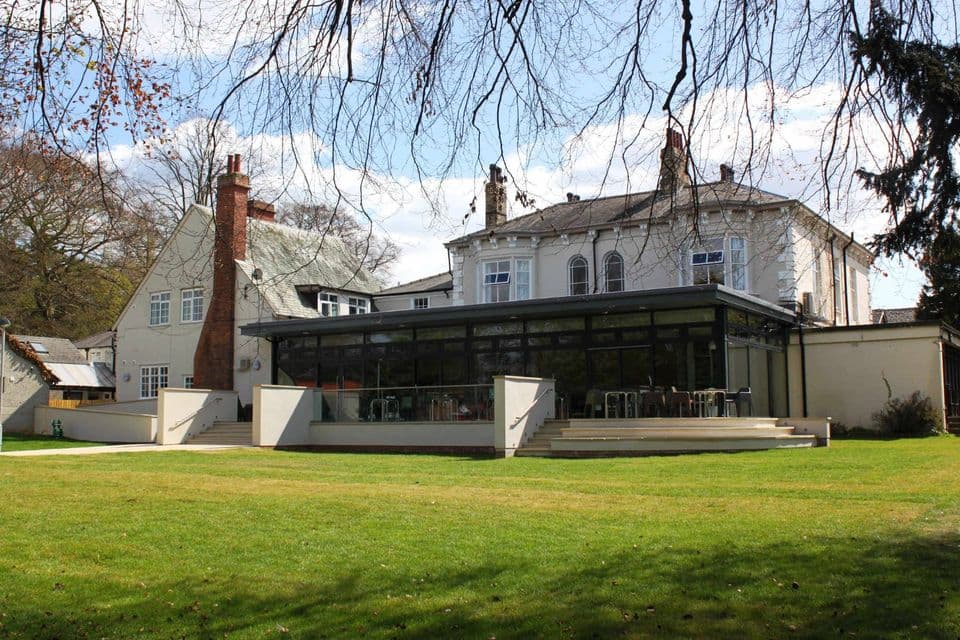 Modern glass extension of YHA York Hostel with a grassy area and trees in the background under a blue sky.
