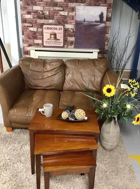 Brown leather sofa with a coffee mug, wooden nesting tables, and a vase with sunflowers and decorative items.