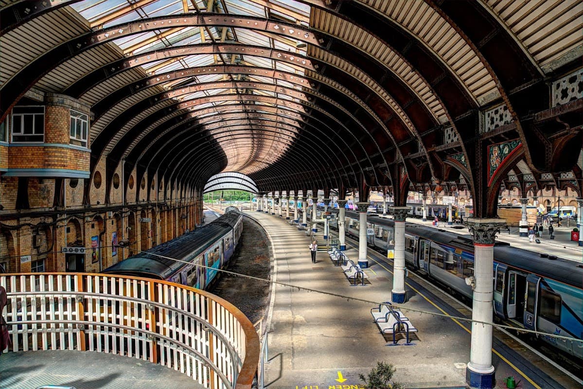 Historic train station with arched glass roof, platforms, and trains, showcasing architectural details and waiting areas.