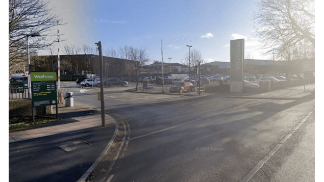 Car park entrance with signage for Waitrose, vehicles parked, and trees lining the area in York, Yorkshire.