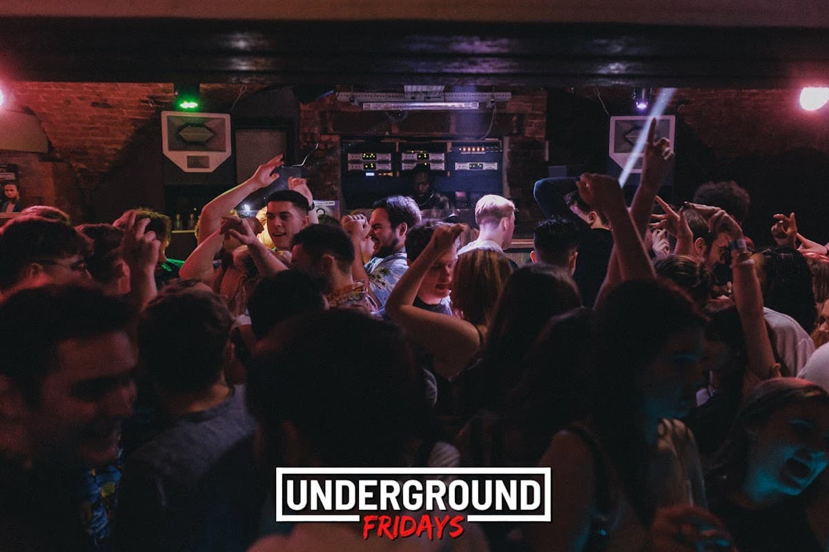 Crowded nightclub scene with people dancing and a DJ in the background, vibrant lights illuminating the atmosphere.