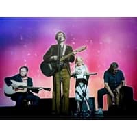 Band Pulp performing on stage with guitars and drums against a vibrant pink and purple backdrop.