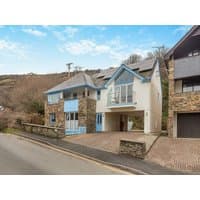 "Starfish" holiday cottage with stone facade, blue trim, balcony, and sloped roof, nestled in a hilly landscape.