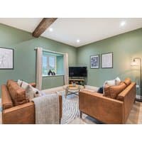 Cozy living room with two brown leather sofas, green walls, wooden beam, TV, and window with countryside view.